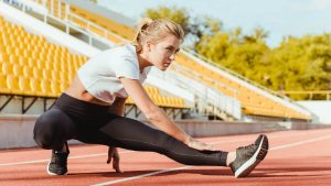 Mulher loira alongando a perna em pista de atletismo