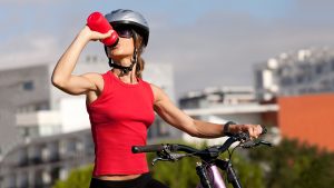 Mulher com capacete bebendo água enquanto anda de bike pela cidade